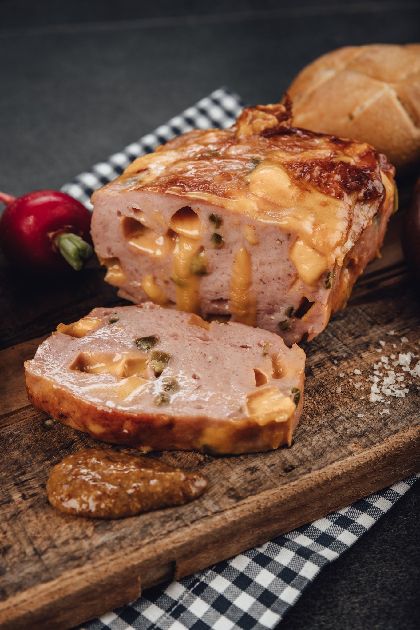 Aufgeschnittener Donlicate Fleischkäse mit Cheddar und Jalapeño auf einem Holzbrett, mit Brötchen und Senf