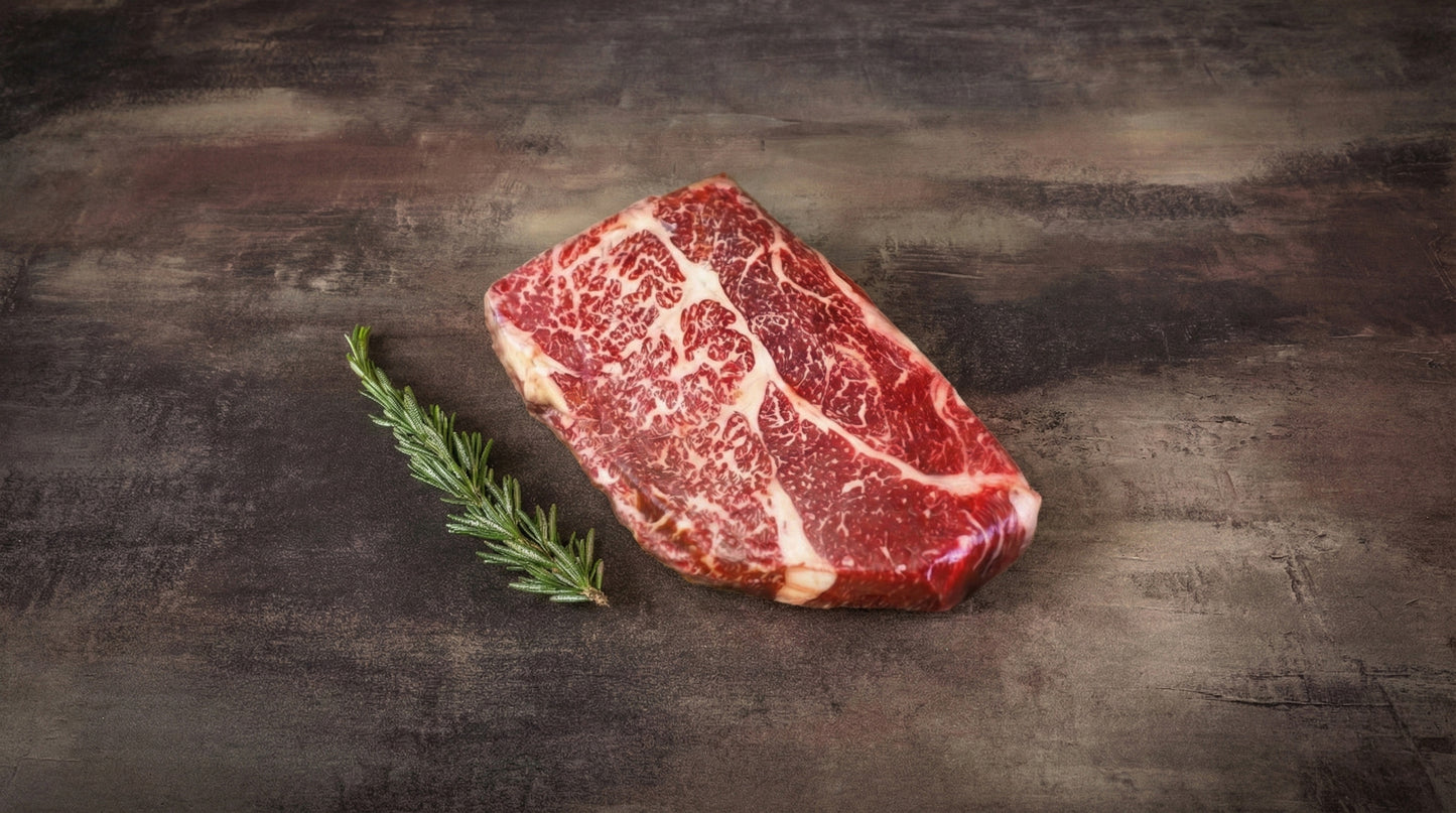Wagyu Chuck Steak, roh und stark marmoriert, auf dunklem Stein mit Rosmarinzweig