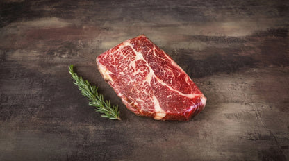 Wagyu Chuck Steak, roh und stark marmoriert, auf dunklem Stein mit Rosmarinzweig