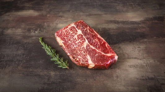 Wagyu Chuck Steak, roh und stark marmoriert, auf dunklem Stein mit Rosmarinzweig