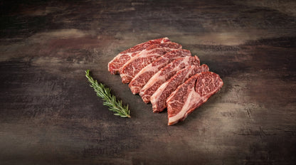 Aufgefächerte Scheiben Wagyu Tataki Steak, stark marmoriert, auf dunklem Stein mit Rosmarinzweig